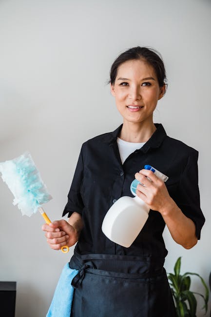 Two professional cleaners from Holborn Carpet Cleaners are conducting surface cleaning and maintenance in a modern kitchen with a minimalist design. The female cleaner is vacuuming the light wooden fl